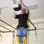 Man standing on a ladder fixing a mechanical garage door opener